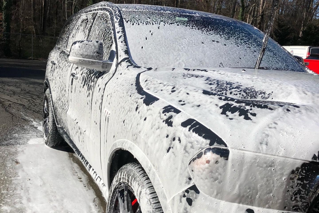 A white SUV is completely covered in thick foam during a hand wash, illustrating the recommended cleaning process for maintaining Paint Protection Film and demonstrating Caring for Your PPF with gentle, pH-balanced products.