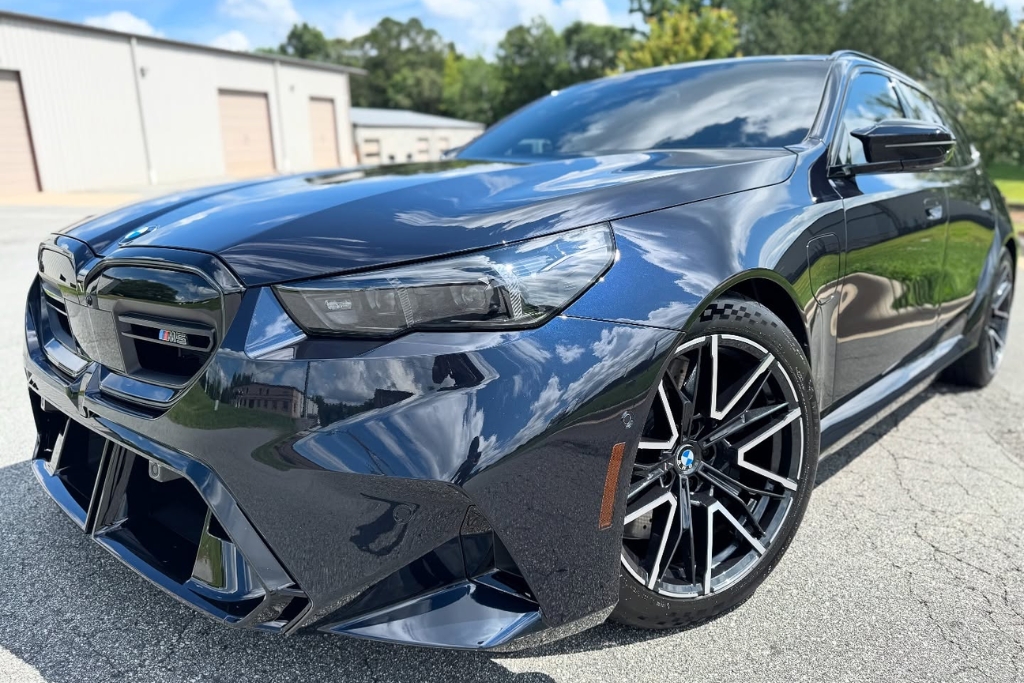 A glossy black BMW M5 with a flawless, high-shine finish sits outdoors under sunlight, showcasing the Benefits of PPF such as preserved paint, enhanced aesthetics, and protection from environmental damage.