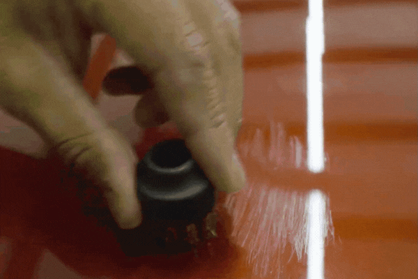 A close-up of a hand using a small abrasive brush on a red vehicle’s surface shows how Paint Protection Film resists scratches, helping answer What Is PPF by illustrating its durability and self-healing properties.