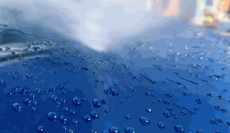 Water beads up and rolls off the surface of a blue car, demonstrating the hydrophobic effect after ceramic coating has been applied.