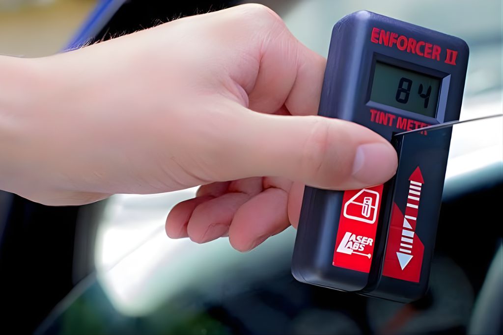 Close-up of a hand holding an Enforcer II tint meter showing a reading of 84 percent visible light transmission, used to verify legal window tinting on a vehicle in North Carolina.
