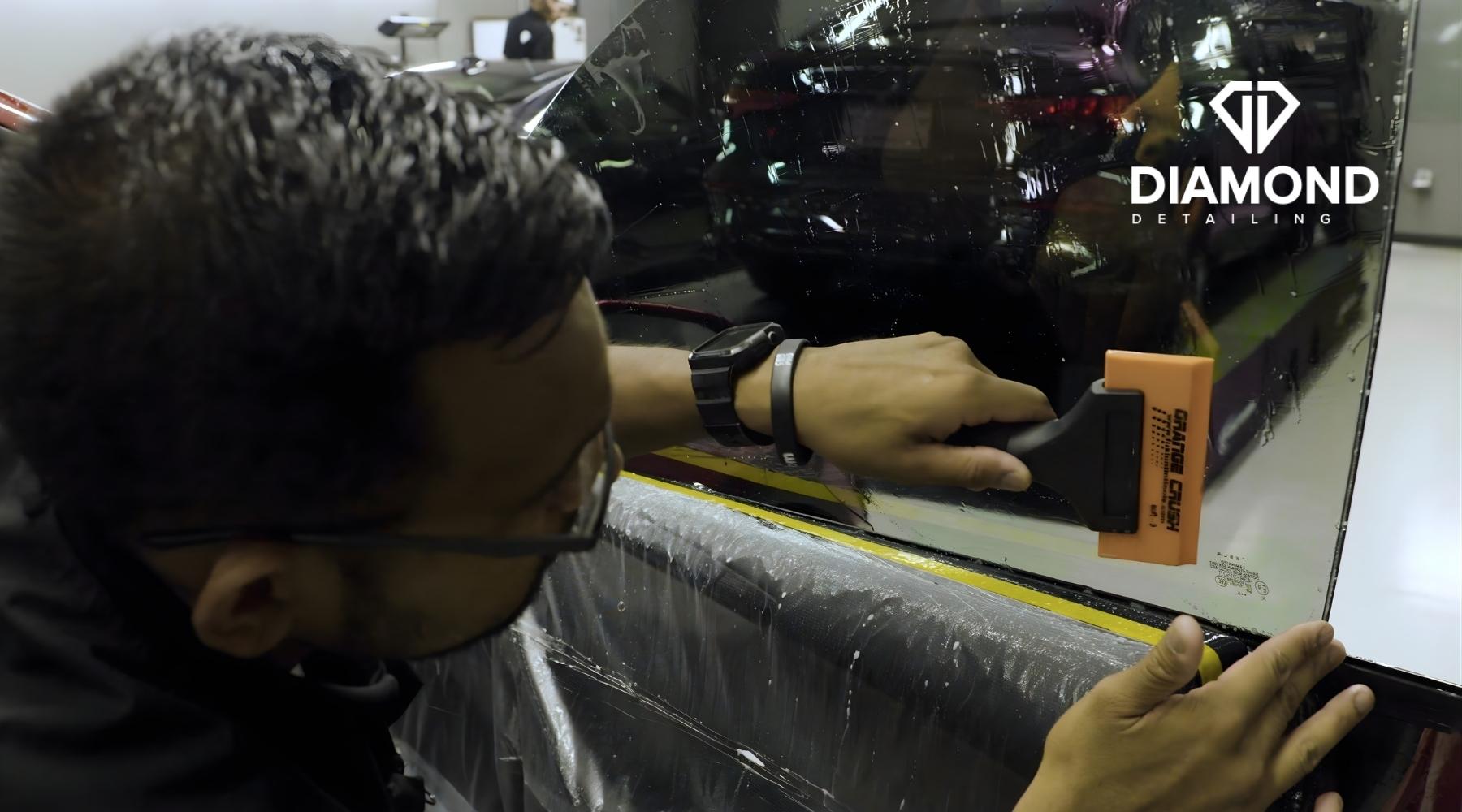 A Diamond Detailing technician in Troutman, NC uses a squeegee to smooth a freshly applied tint film on a car window, showing a key step in What Is Automotive Window Tinting.