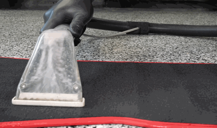 Close-up of an extractor nozzle deep cleaning a black car floor mat with red trim, used in mobile detailing.
