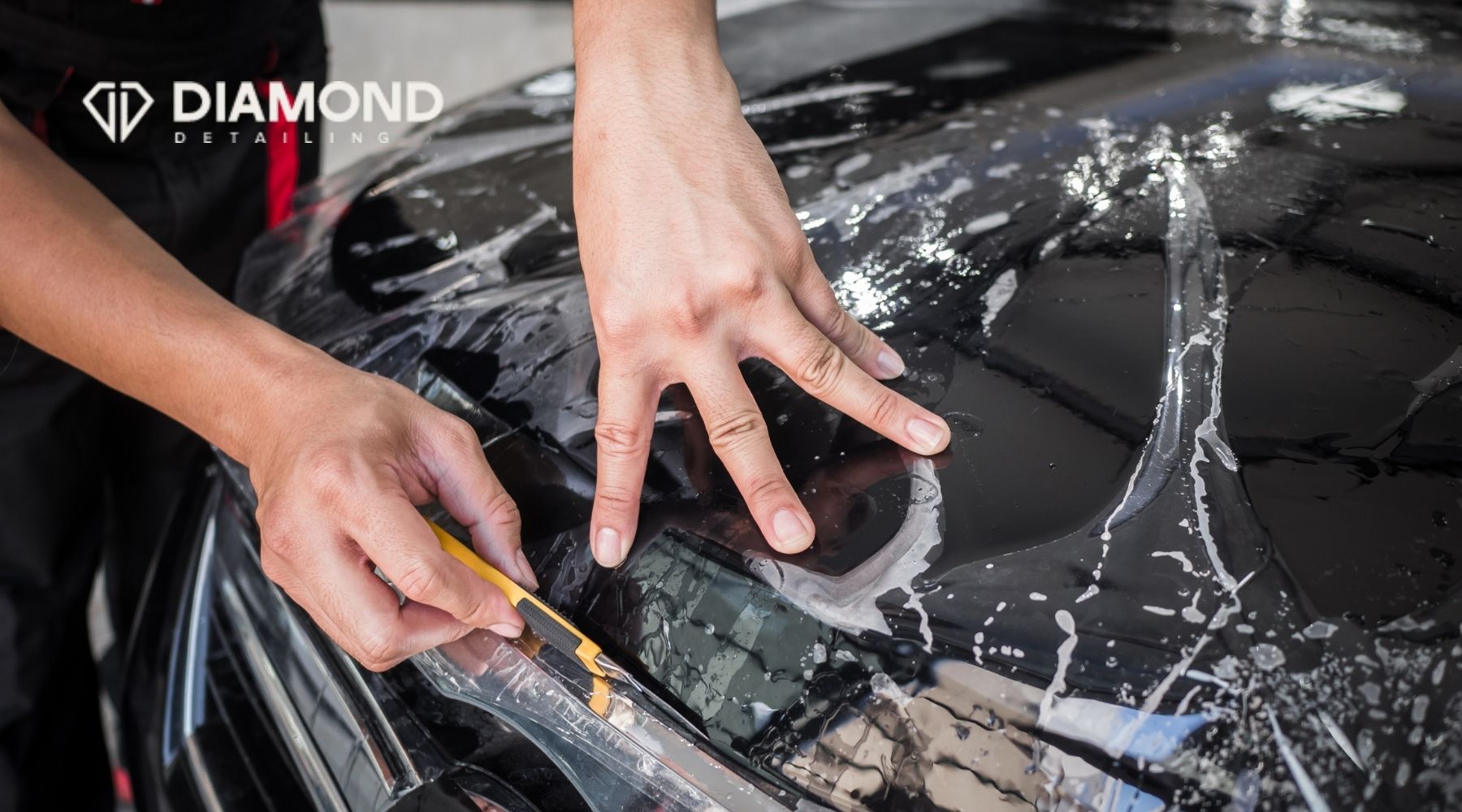 Technician installing paint protection film on a black car hood during professional PPF application.