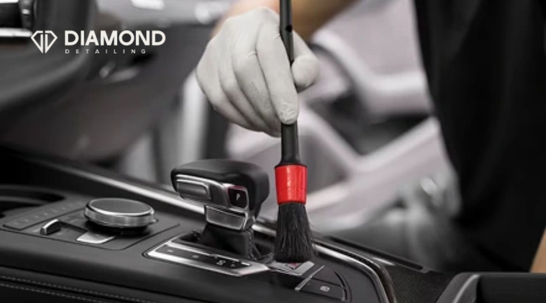 Professional auto detailer cleaning a car’s center console with a detailing brush at Diamond Detailing.