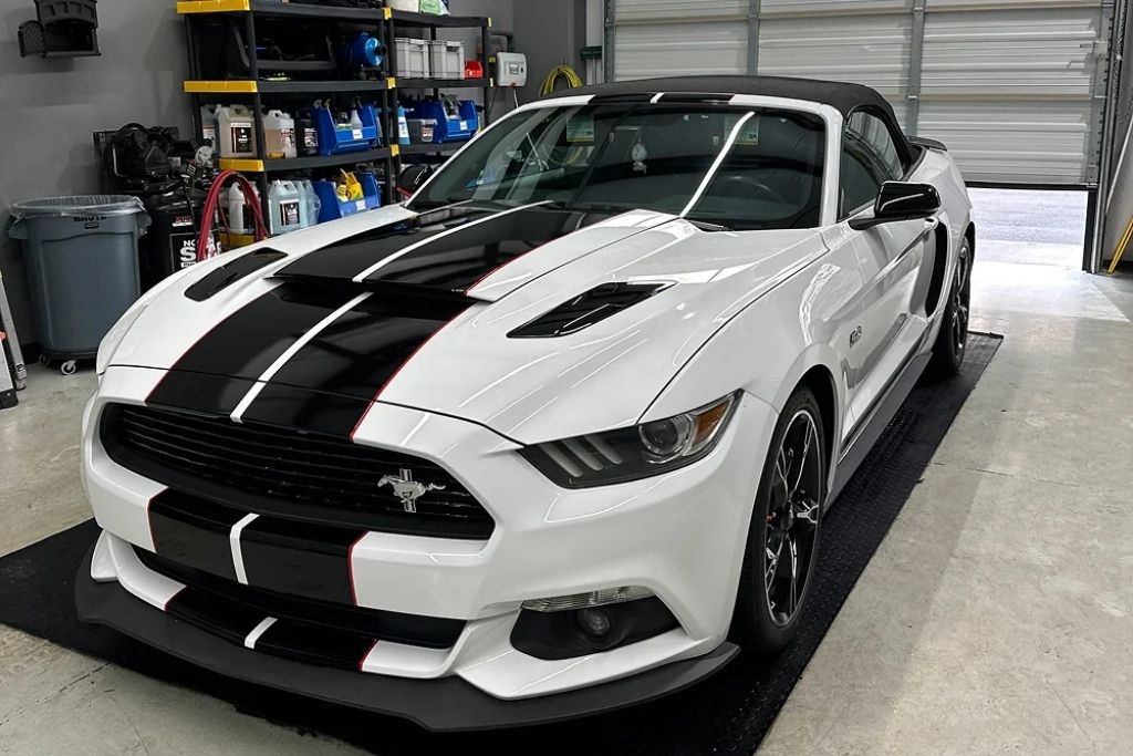 White Ford Mustang with black racing stripes inside detailing shop after paint protection film installation.
