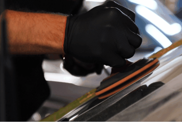 Technician applying paint protection film to a vehicle surface using a squeegee during professional auto detailing.