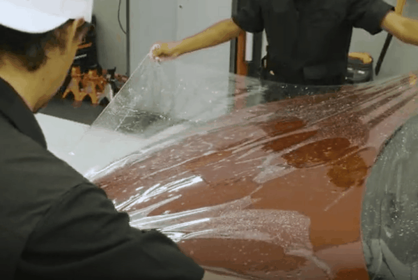 Technicians applying clear paint protection film to a vehicle hood during professional PPF installation.