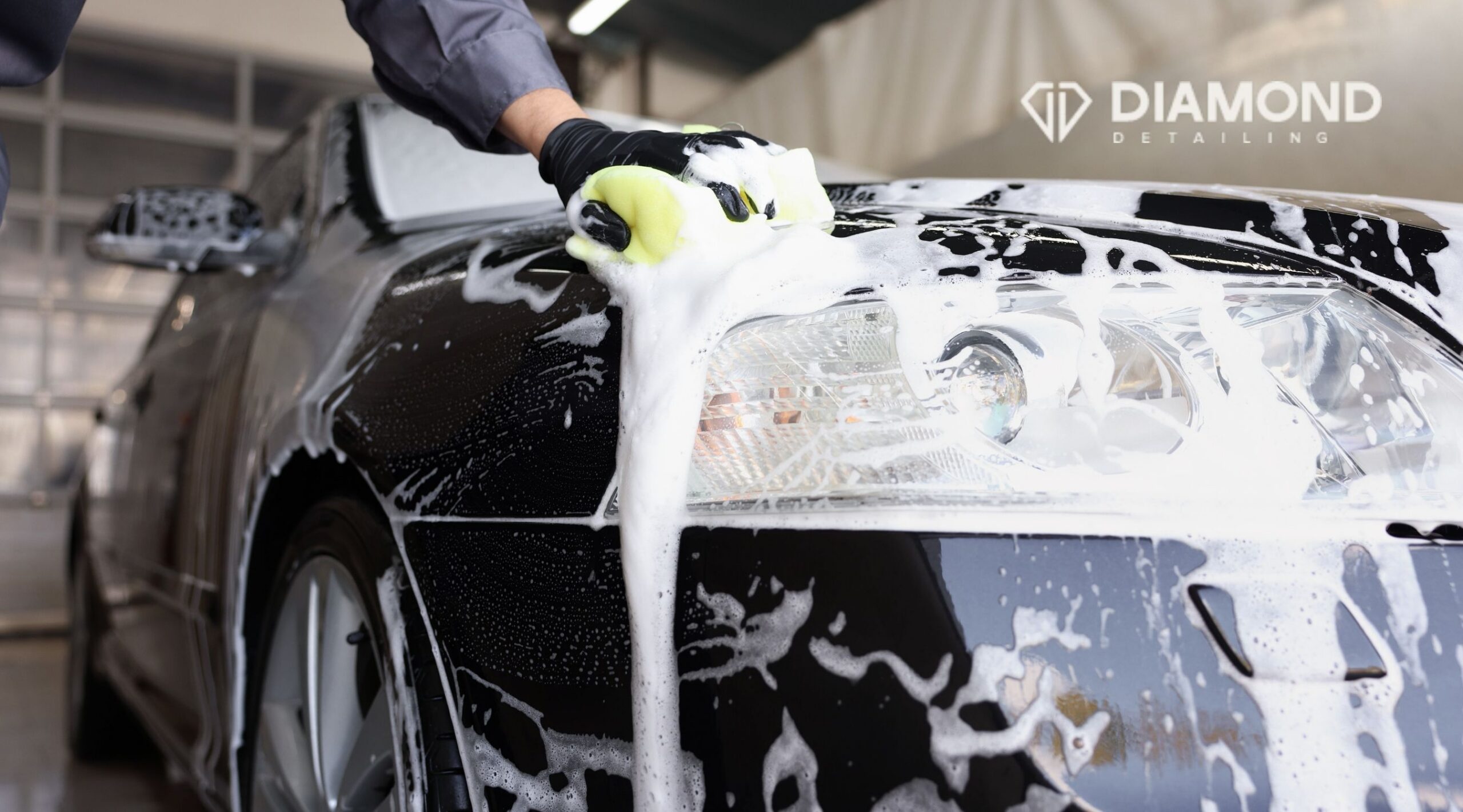 Professional auto detailer hand washing a black car covered in foam at Diamond Detailing