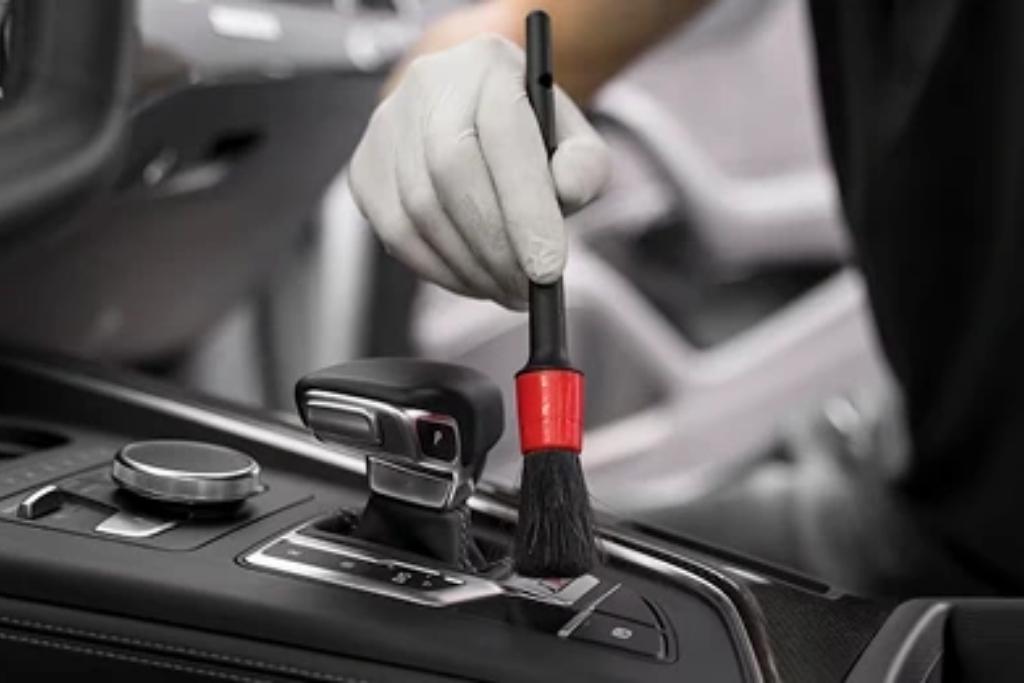 Technician using a detailing brush to clean the center console of a car interior