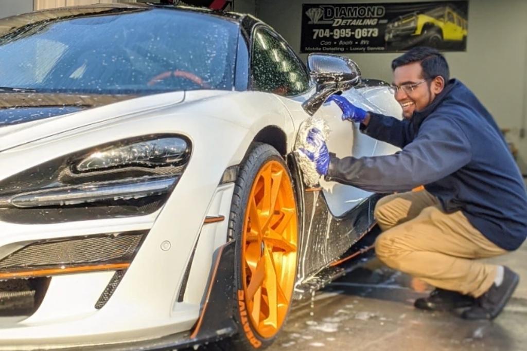 Detailer hand-washing a white sports car with orange wheels at Diamond Detailing