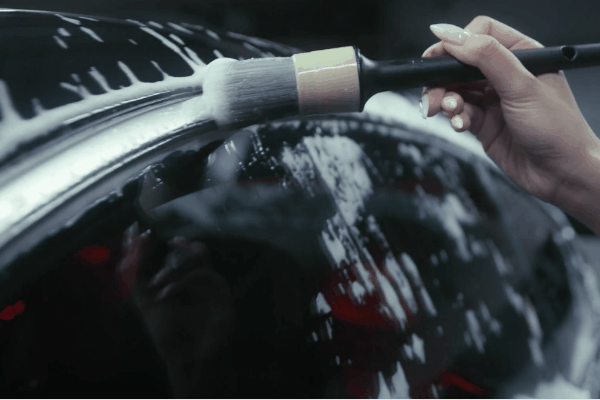 Detailer using a soft brush to clean around a car window trim during exterior auto detailing
