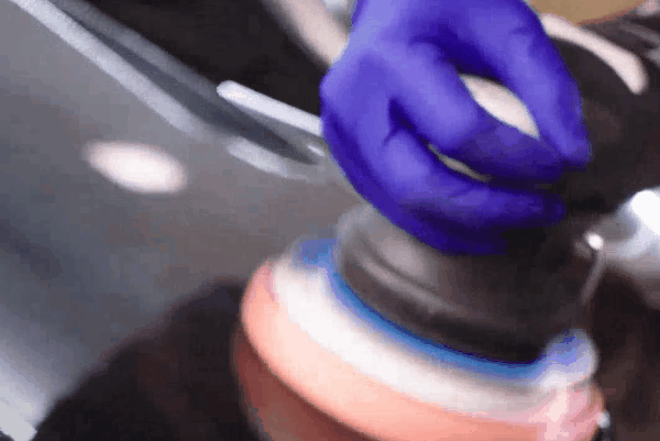 Man polishing the headlight of a black car with a cloth.