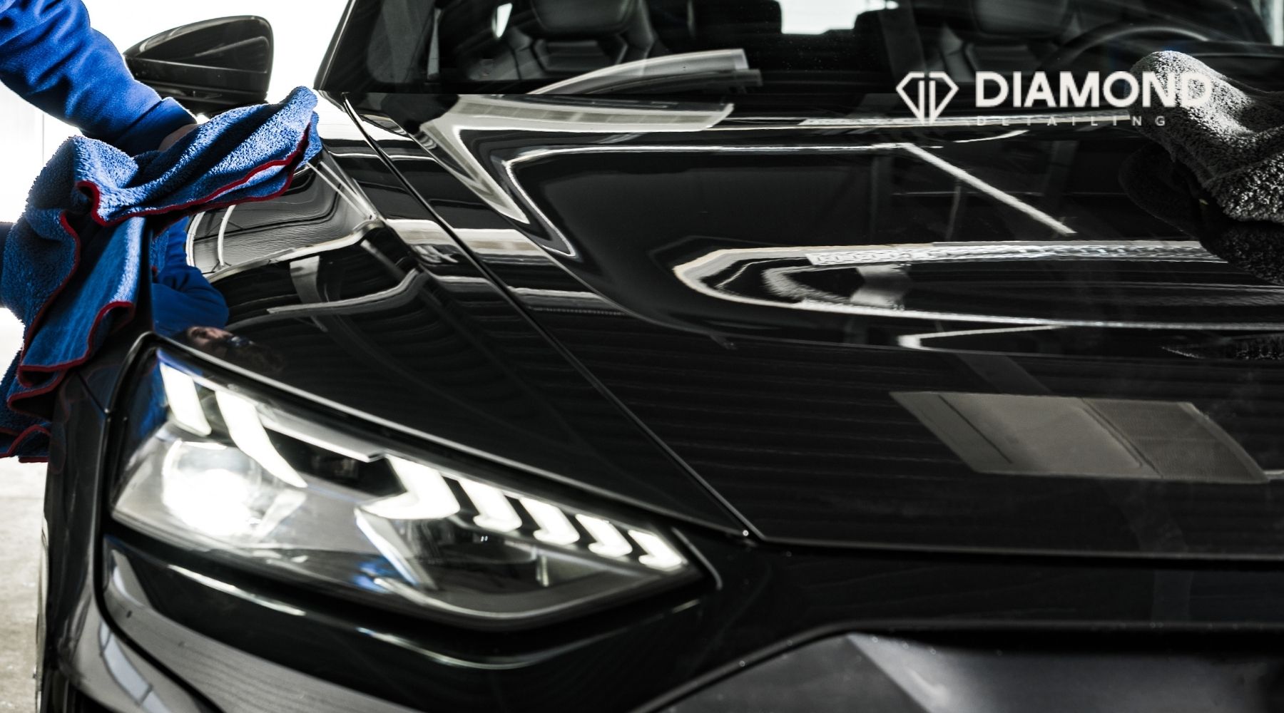 Technician wiping the hood of a black car during a professional mobile detailing service