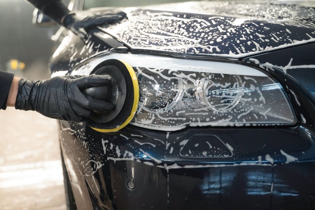 Close-up of a car headlight and hood being hand washed during a professional auto detailing service