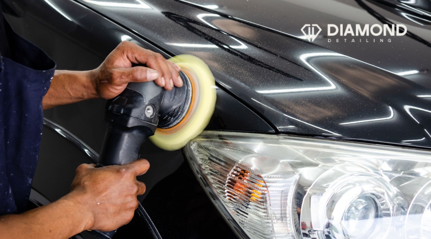 Technician polishing the front panel of a black car with a machine buffer at Diamond Detailing