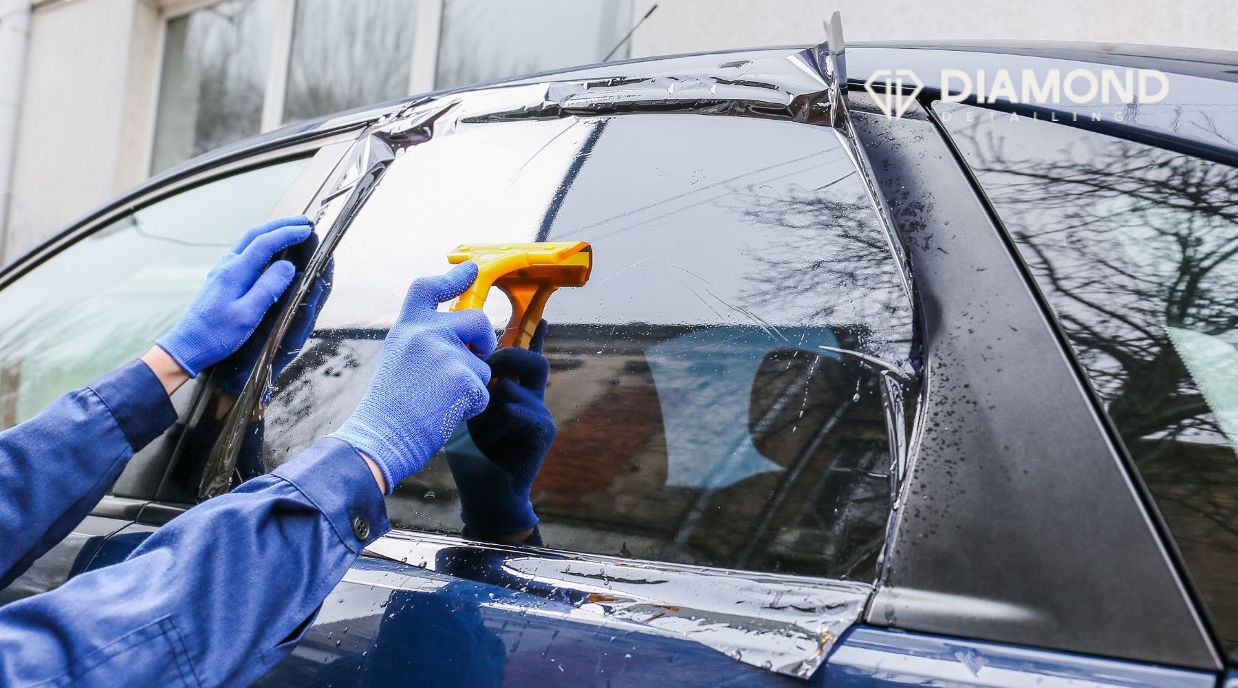 Technician applying window tint film to a car side window during professional installation