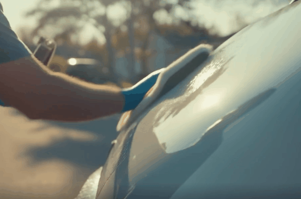 Person hand-washing a white car with a microfiber mitt during an exterior detailing service