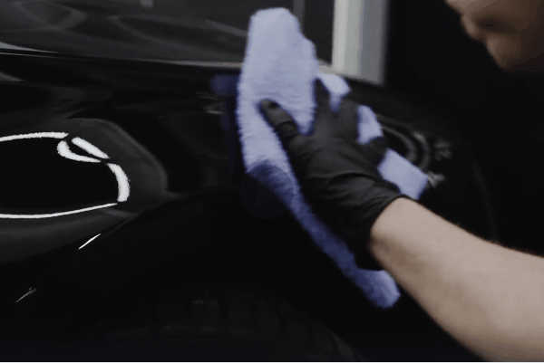 Detailer wiping a black vehicle with a microfiber towel during a professional detailing service
